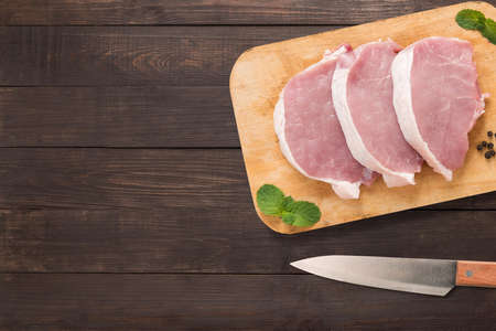 Top view raw pork chop steak on cutting board and knife on wooden background. Copyspace for your text.の写真素材