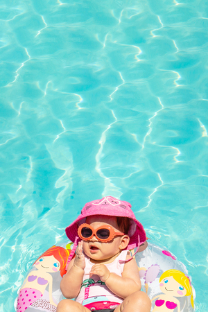Beautiful Baby Girl Wearing Hat and Sunglasses On A Float In Clear Waterの写真素材