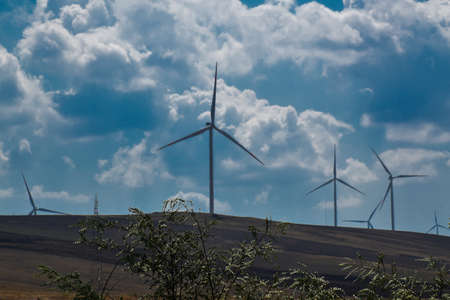 Big wind turbines against an intense blue sky with many clouds.