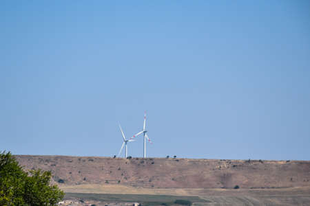 Barren hilly landscape with several wind turbines under a blue sky.