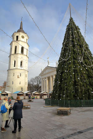 VILNIUS, LITHUANIA - DECEMBER 28, 2016: Women having a drink in front of a Christmas tree on Cathedral Square with The Belfry (Cathedral Clock Tower) and the Cathedral in the backgroundのeditorial素材
