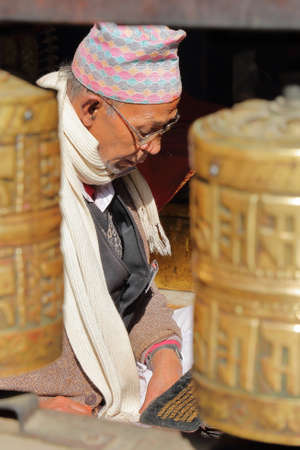 PATAN, NEPAL - DECEMBER 19, 2014: A Nepalese man reading Bhudist prayers at the Golden Temple with prayer wheels in the foregroundのeditorial素材