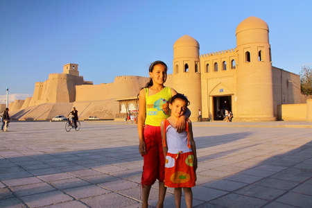 KHIVA, UZBEKISTAN - MAY 6, 2011: Two Uzbek little girls posing in front of the city walls of Khiva at sunsetのeditorial素材