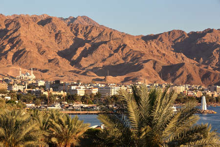 General view of the town of Aqaba at sunset with Palm trees in the foreground and mountains in the...
