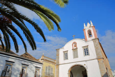 The church Nossa Senhora da Ajuda ou de Sao Paulo, located on Antonio Padinha Square, with historical buildings in the foreground, Tavira, Algarve, Portugalの写真素材