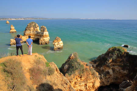 LAGOS, PORTUGAL - NOVEMBER 14, 2018: Two tourists overlooking cliffs, rocks formations and clear water viewed from Ponta da Piedadeのeditorial素材