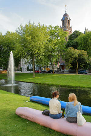 ROTTERDAM, NETHERLANDS - MAY 31, 2019: Two young women relaxing along Westersingel canal on Mauritsweg street, with the Clock Tower of Oud Katholieke Paradijskerk church in the backgroundのeditorial素材