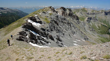 Hiking along a mountain ridge overlooking the two valleys of Saint Veran and Ceillac (Cristillan), with a montain range covered with snow (with Mount Pelvoux) in the background, Queyras Regional Natural Park, Southern Alps, Franceの写真素材