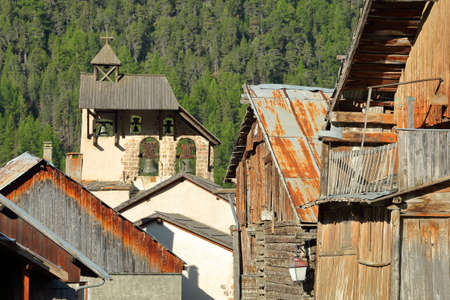 Traditional wooden houses with the bell tower of Saint Sebastien Church in the background, Ceillac,...