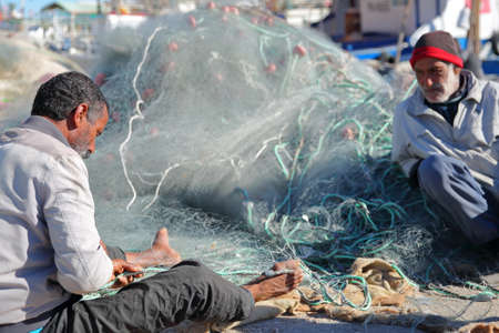 MAHDIA, TUNISIA - DECEMBER 26, 2019: A fisherman repairing his net at the fishing portのeditorial素材