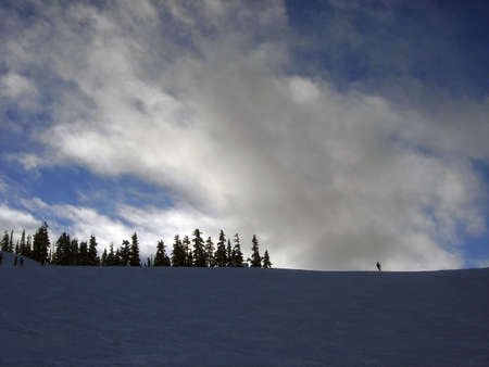 Lonely skier on a ridge of a ski slope with blue sky and cloudsの写真素材