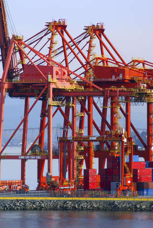 Cranes in red at an industrial port with a bridge in the backの写真素材