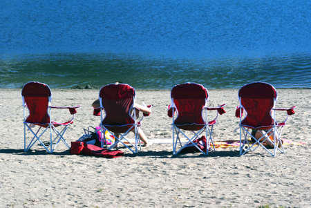 People relaxing and sunbathing in a row of beach chairs on the sand in front of the ocean on a sunny summer dayの写真素材