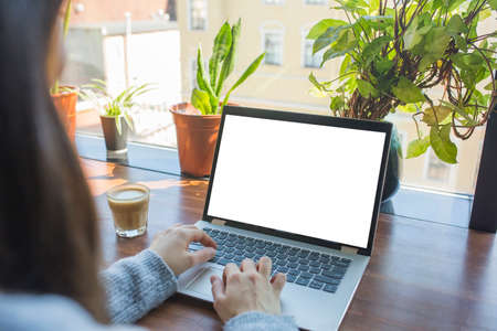 Mockup image of woman using laptop with blank white desktop screen while drinking coffee. Back view,...