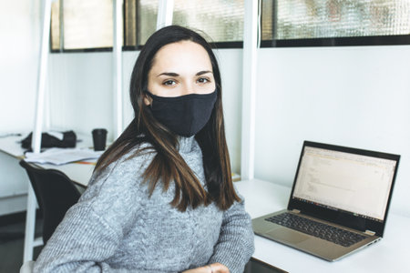Young woman with face mask at work in office. Safety working during pandemic time.の写真素材