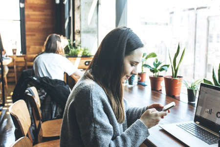 A beautiful adult girl uses a cell phone and laptop.の写真素材