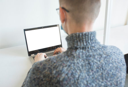 Man in protective face mask working on laptop computer. Screen of computer with copy space. Mockup template.の写真素材