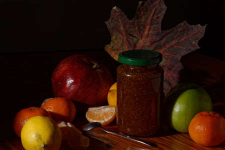 Still life photo of jar of homemade strawberry sugar sauce and a spoon with various fruits on a...