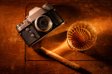 Vintage film camera, whiskey, and cigar on warm wooden surface. Evokes nostalgia, relaxation, and hobbies like analog photography and fine spirits. Ideal for vintage, leisure, and masculine themes.の写真素材