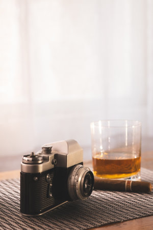Retro-style composition featuring a classic camera alongside a whiskey glass and cigar on a textured surface, evoking a nostalgic and sophisticated atmosphere.の写真素材