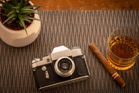 Styled composition showcasing a vintage camera next to a glass of whiskey, a cigar, and a potted plant, illustrating retro aesthetics and refined hobbies.の写真素材