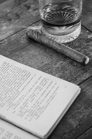 Centered monochrome photo: book, cigar, glass on wood. Nostalgic, classic still life. Contrasting textures, vintage vibe.の写真素材