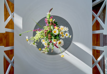 Overhead shot of a bouquet of colorful wildflowers in a vase on a white table with dramatic natural light and shadows. Artistic composition and minimalistic styleの写真素材