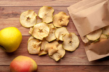Healthy snack. Homemade dehydrated apple chips and fresh apples on a rustic wooden backgroundの写真素材