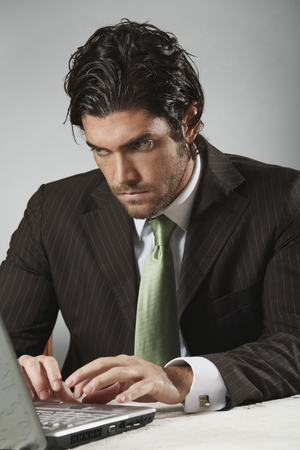 Handsome businessman looks at portable computer with determined expressionの写真素材
