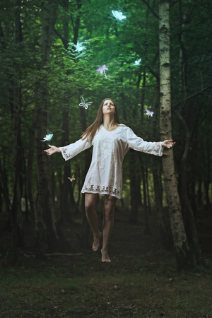 Beautiful woman flying among strange butterflies in a forest . Fantasy and surreal の写真素材