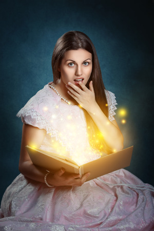 Beautiful girl with shocked expression and fairy tale magical bookの写真素材