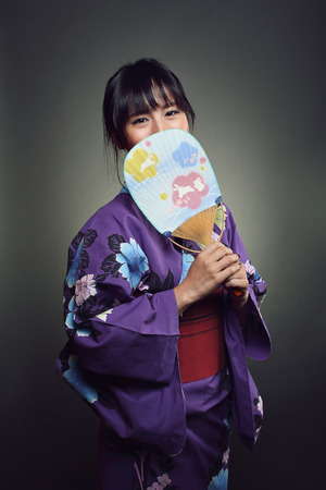 Beautiful japanese woman smiling behind oriental fan . Studio shotの写真素材