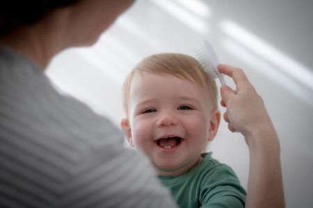 Mother brushing smiling toddler's hairの写真素材