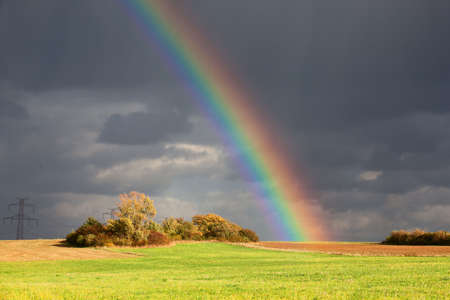 Natural rainbow over green field and dark skyの写真素材