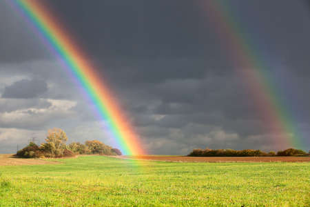 Natural two rainbow over green field and dark skyの写真素材