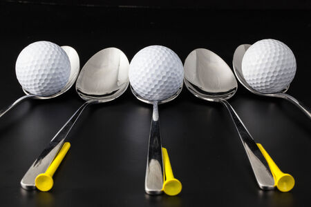 Spoons and different golf balls on a black tableの写真素材
