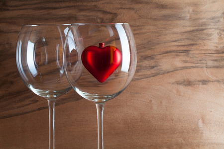 Two glasses  of wine and red heart on the wooden background from real wood veneer with interesting growthの写真素材