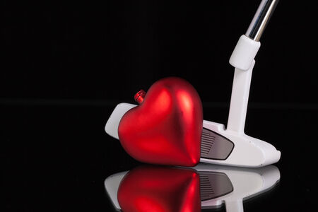 Golf putter and red heart on the black glass deskの写真素材
