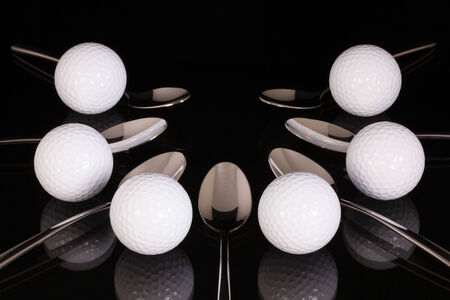 Teaspoons and golf equipments on the black glass deskの写真素材