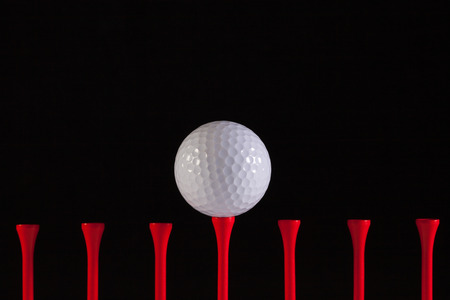 Golf ball and red tee on a black backgroundの写真素材