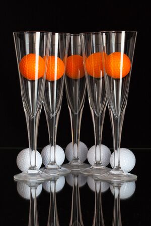 Five glasses of champagne, white and orange golf balls on the glass plateの写真素材