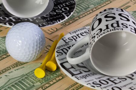 Two empty coffee cups and golf equipments lying on US dollar banknotesの写真素材