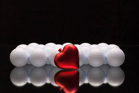 White golf balls and red heart on a glass plateの写真素材