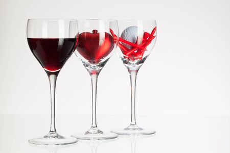 Wine glasses with red wine, heart and golf ball on white tableの写真素材