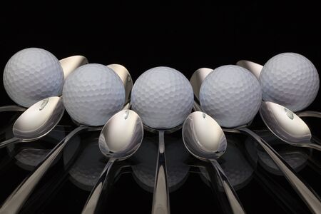 Golf balls and nine spoons on a black glass deskの写真素材