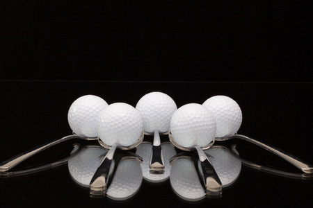 Five spoons and golf balls on a black glass deskの写真素材