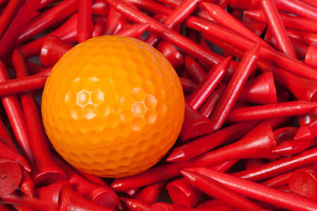 Orange  golf ball lying between red wooden golf teesの写真素材