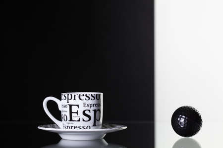 White cup of coffee and black golf ball on a glass deskの写真素材