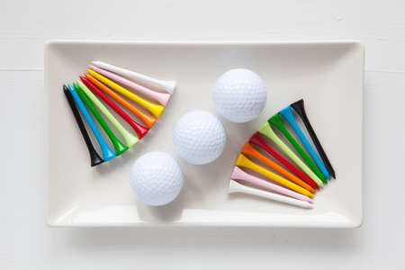 White ceramic dishes with golf balls and wooden tees on over white background, rectangle dishの写真素材