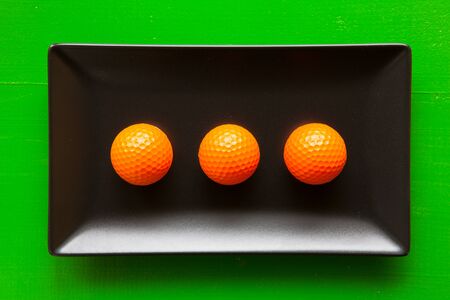 Black ceramic dishes with golf balls on over green background, rectangle dishの写真素材